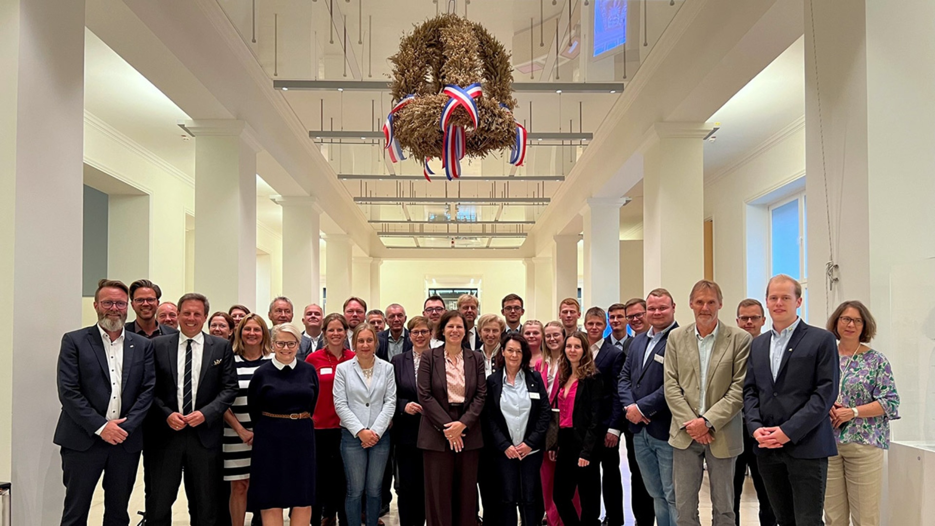 Gruppenfoto mit der Landjugend und Landespolitikern, die unter der in der Eingangshalle hängenden Erntekrone stehen.