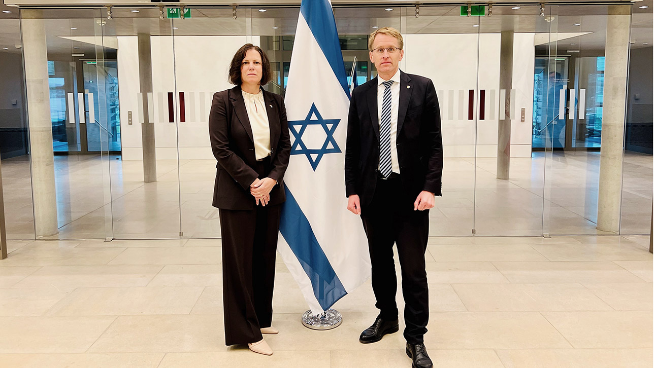 Ministerpräsident Daniel Günther und Parlamentspräsidentin Kristina Herbst stehen vor einer Israel-Flagge im Landtag.