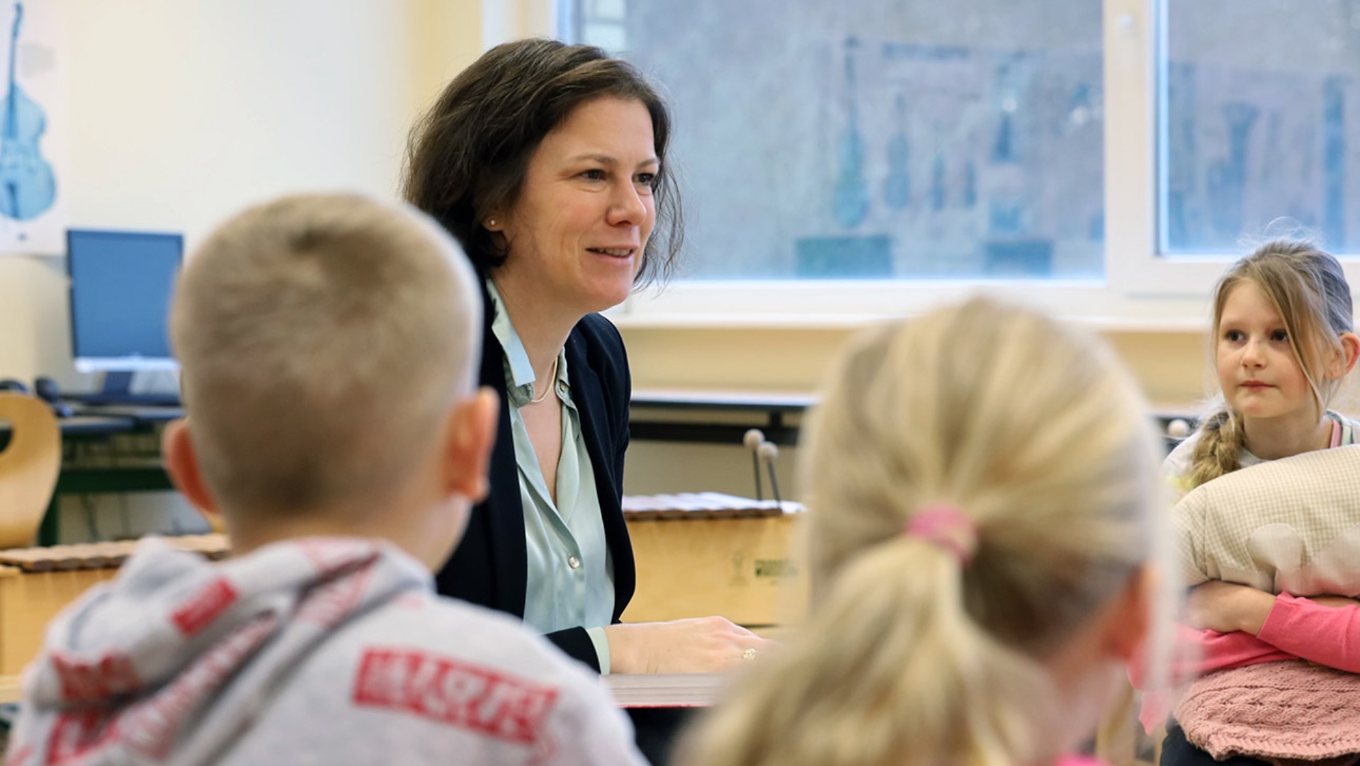 Landtagspräsidentin Kristina Herbst liest umgeben von drei Kindern aus einem Buch vor.