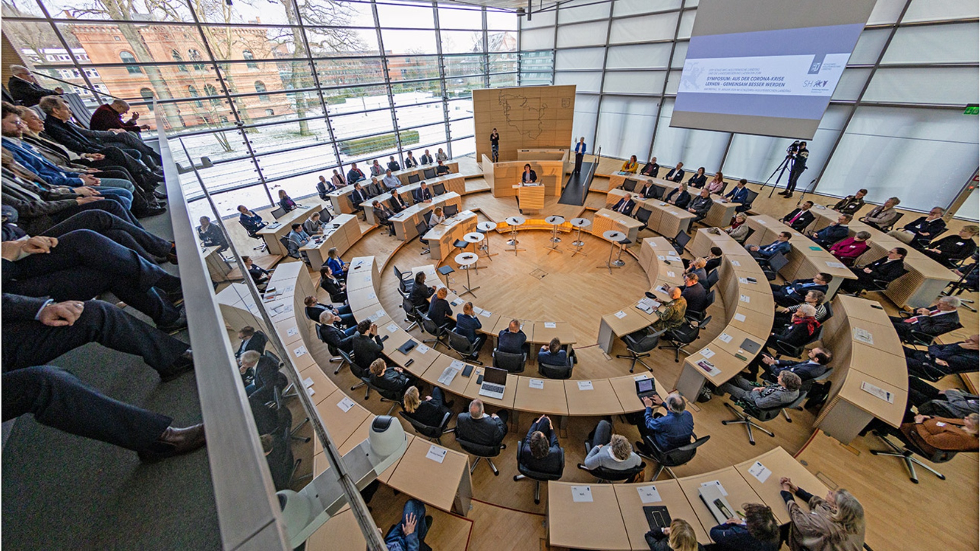 Blick von der Besuchertribüne auf den vollbesetzten Plenarsaal zu Beginn des Symposiums "Aus der Corona-Krise lernen – gemeinsam besser werden".