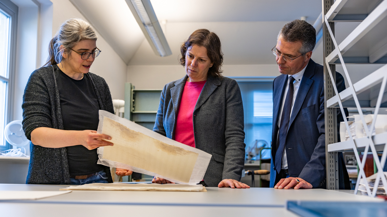 Chefrestauratorin Rebecka Thalmann zeigt Landtagspräsidentin Kristina Herbst und Landtagsdirektor Prof. Utz Schliesky ein fertig restauriertes Dokument.