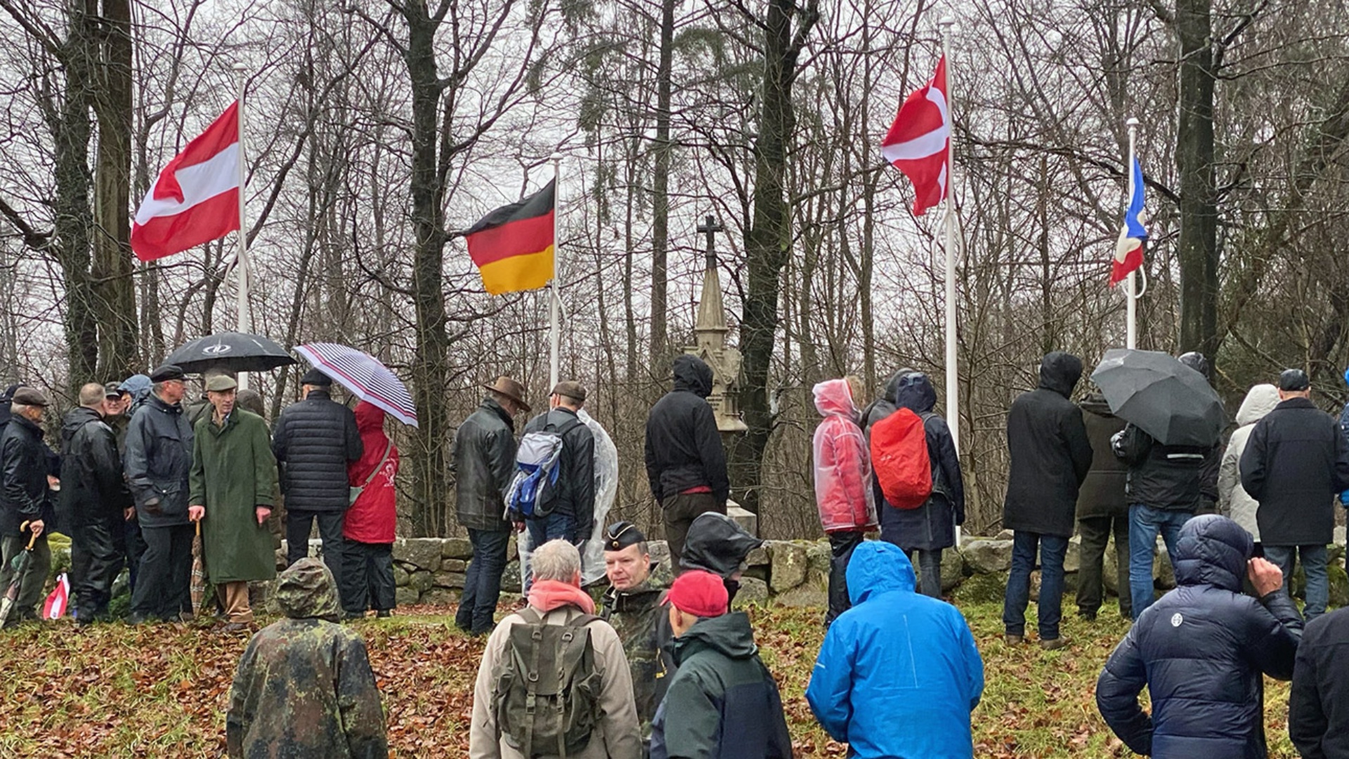 Teilnehmer des Oeversee-Marsches stehen vor dem "Denkmal am Wald", wo 43 gefallene Österreicher und 14 gefallene Dänen bestattet sind.