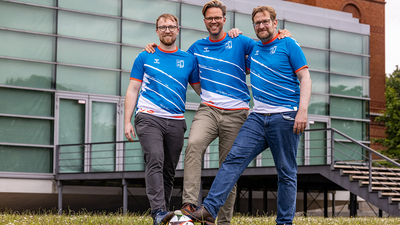 Die Spielführer des FC Landtages, Martin Balasus (CDU) und Jan Kürschner (Grüne), stehen mit dem Vorsitzenden des Europaausschuss Malte Krüger in Trikots und mit den Füßen auf einem Ball vor dem Plenarsaal des Landtages.