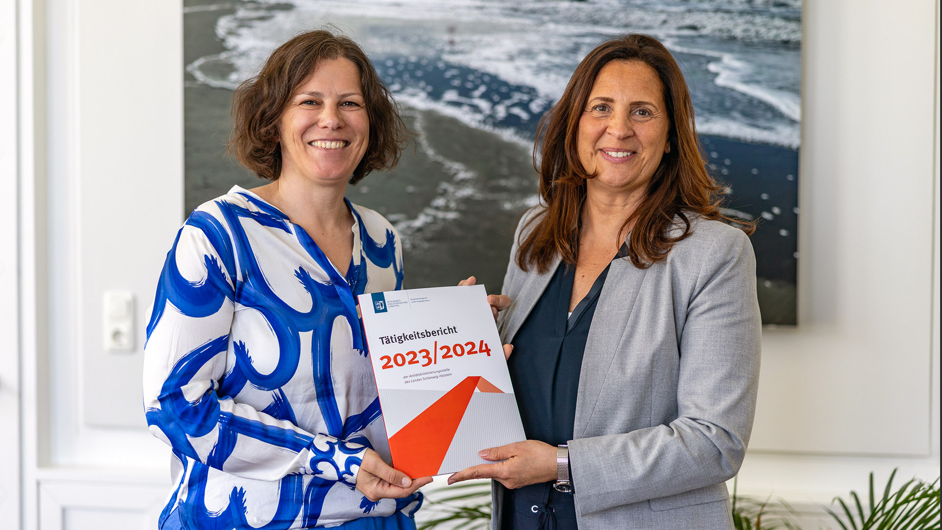 Samiah El Samadoni steht mit Kristina Herbst im Präsidentenzimmer des Landtages. Gemeinsam halten sie den Tätigkeitsbericht der Antidiskriminierungsstelle in den Händen.