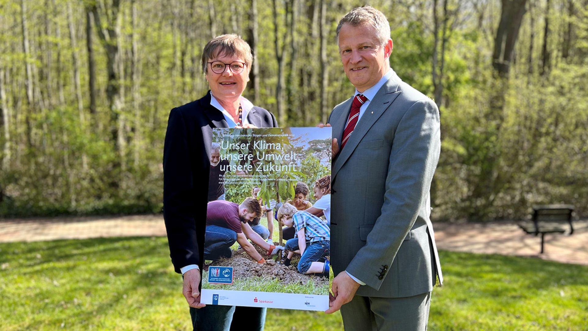 Parlamentsvizepräsidentin Kirsten Eickhoff-Weber und Oliver Stolz, Präsident des Sparkassen- und Giroverbandes für Schleswig-Holstein, halten ein Schild in die Kamera auf dem das diesjährige Motto des Bürgerpreises zu sehen ist. 
