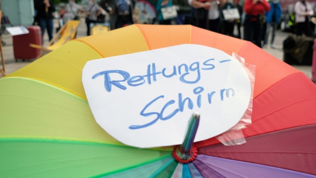 Teilnehmer einer Demonstration spannen einen Regenschirm mit einem Schild "Rettungsschirm" auf.