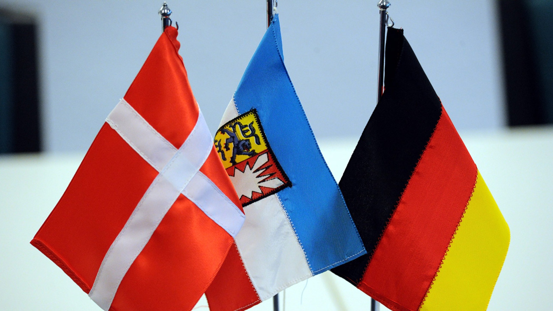 Die Flaggen von Dänemark, Schleswig-Holstein und Deutschland stehen auf einem Tisch.