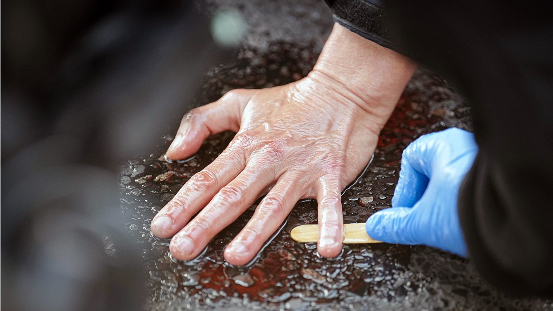 Ein Polizeibeamter löst die Hand eines Klima-Aktivisten vom Asphalt an einem großen Platz in Berlin.