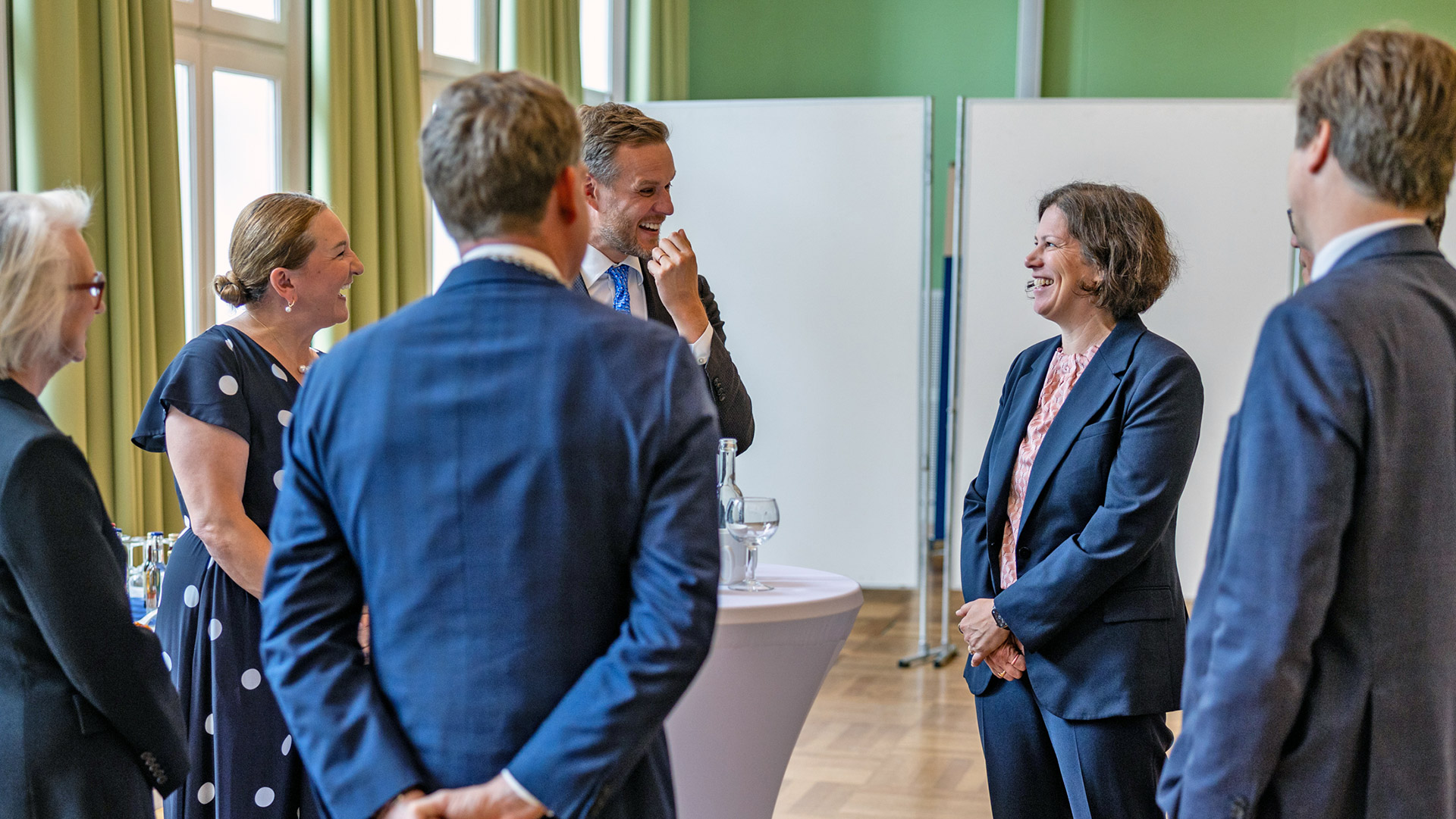 Mehrere Personen stehen an einm Stehtisch und lachen. Im Gespräch sind Landtagspräsidentin Herbst und Gabrielius Landsbergis, der ehemalige Außenminister der Republik Litauen.