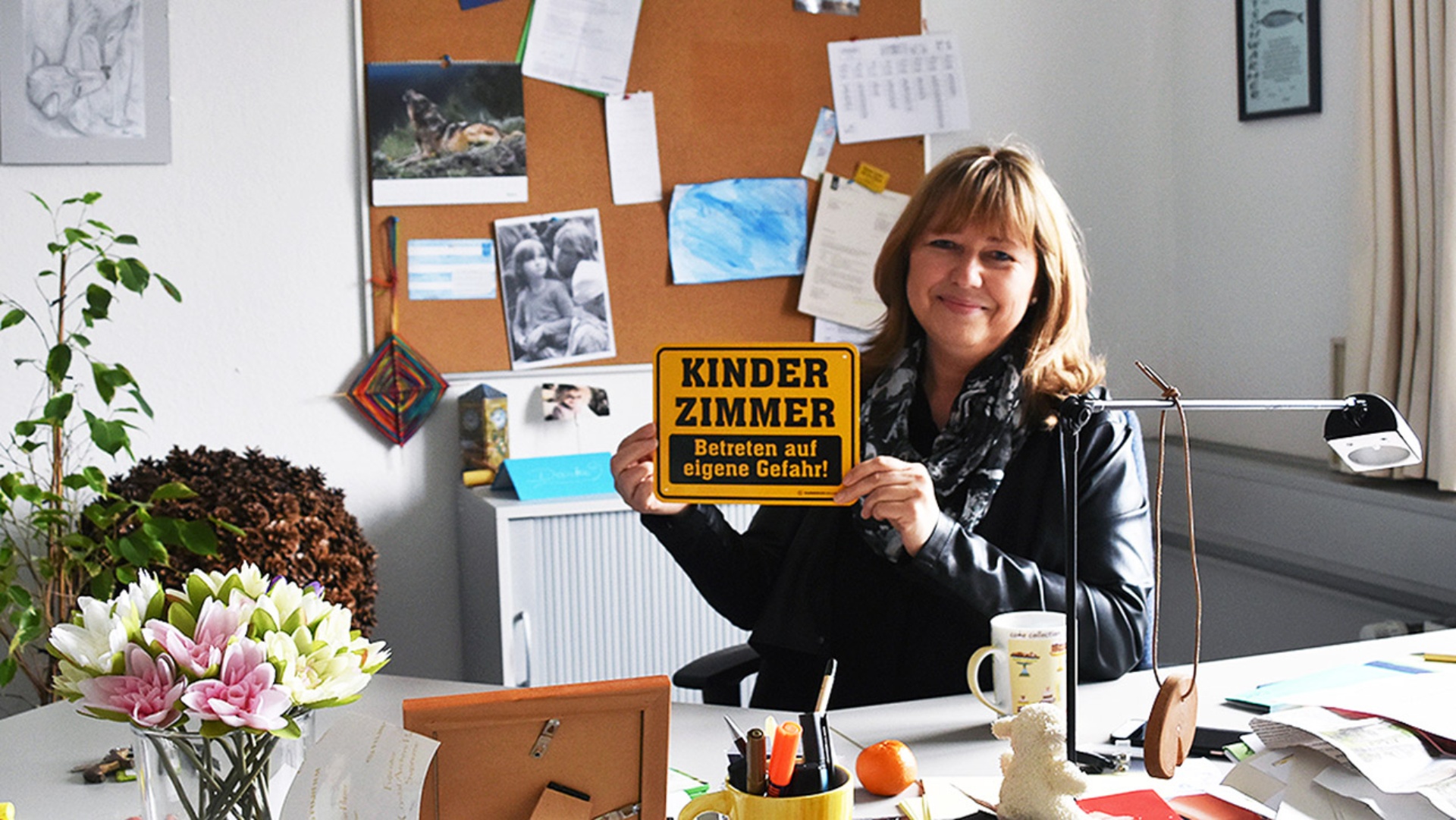 Die SPD-Landtagsabgeordnete Sandra Redmann hält in ihrem Landtagsbürö ein Schild mit der Aufschrift "Kinderzimmer - Betreten auf eigene Gefahr" hoch. 