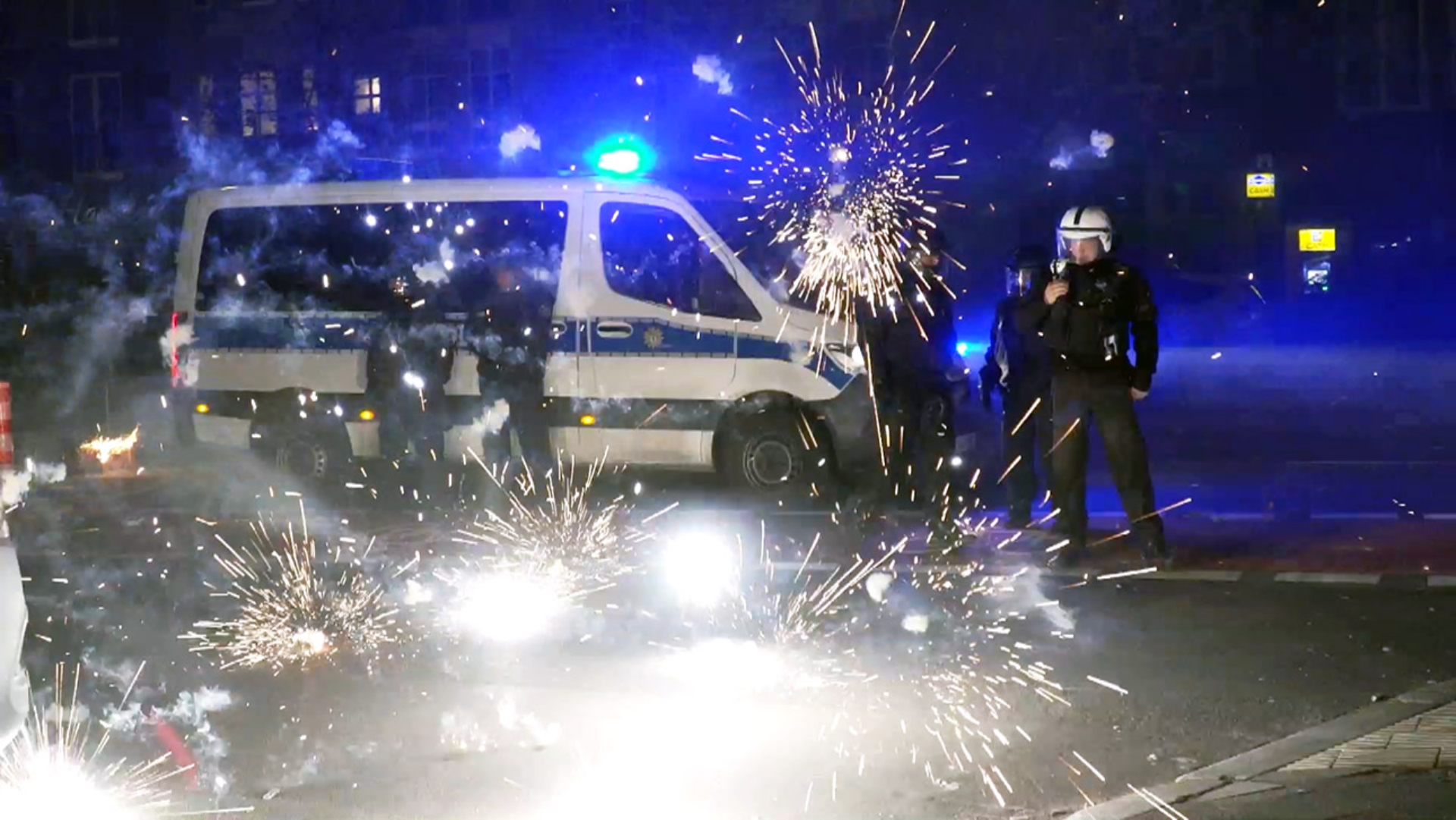 In Berlin stehen Polizeibeamte hinter explodierendem Feuerwerk. 