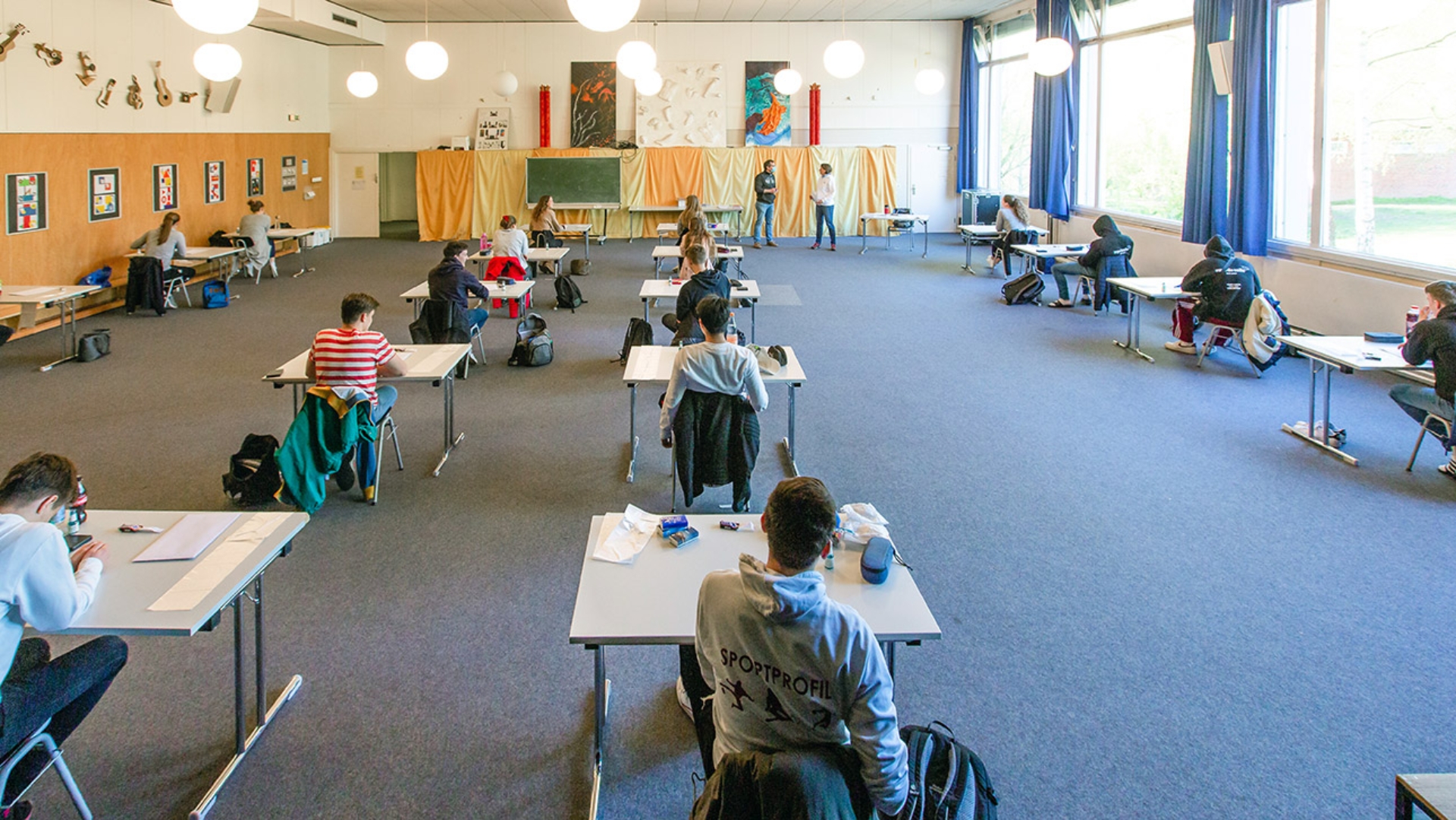 Oberstufen-Schüler der Kieler Max-Planck-Schule sitzen in großem Abstand zueinander in einem Prüfungsraum zu Beginn einer Abiturprüfung.