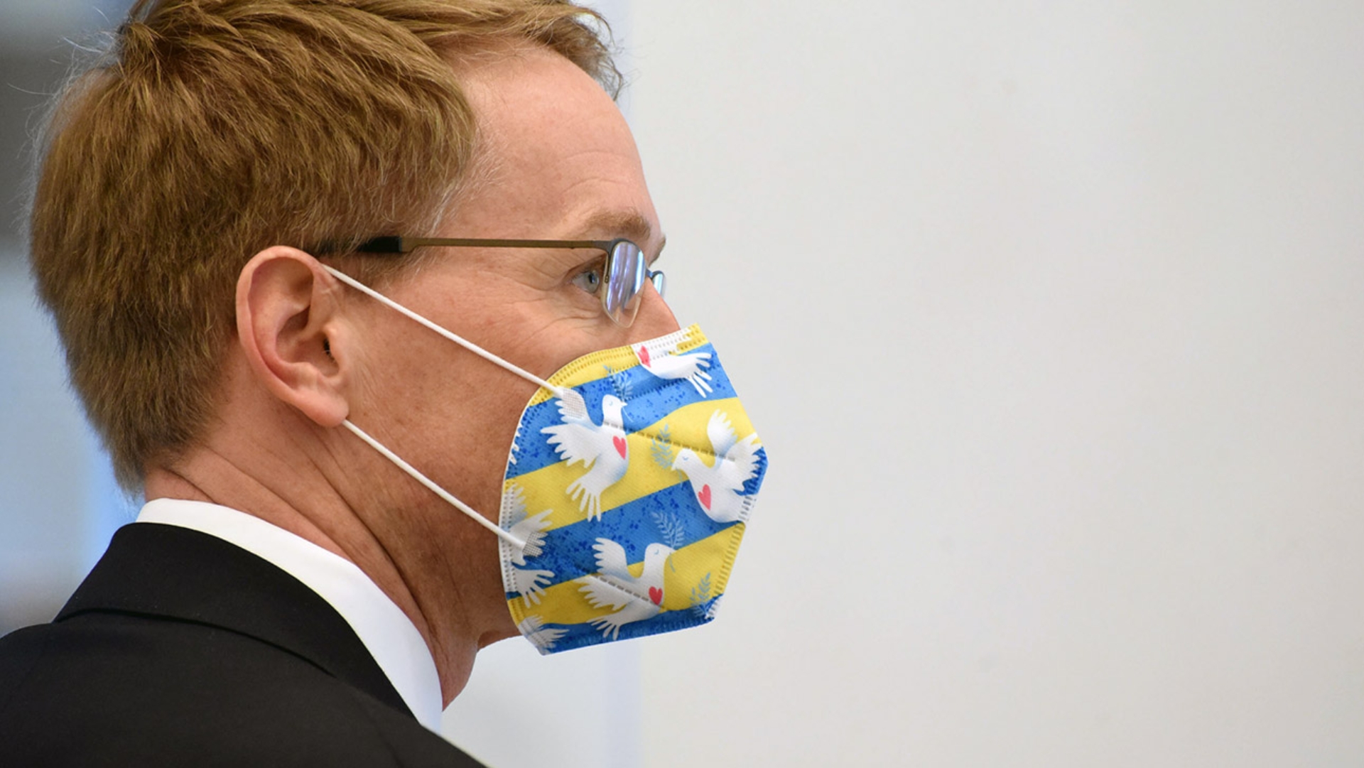 Ministerpräsident Daniel Günther trägt eine Maske in den Farben der Ukraine und mit Friedenstauben.