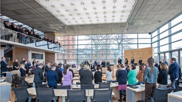 Landespolitiker im Plenarsaal und Gäste auf der Besuchertribüne gedenken stehend der Erdbeben-Opfer.