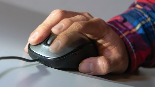 Ein Mann tippt die Linke Taste seiner Computermaus an (Aufnahme mit Blitzlicht und Langzeitbelichtung). 