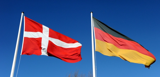 Die deutsche und die dänische Flagge wehen vor blauem Himmel im Wind.