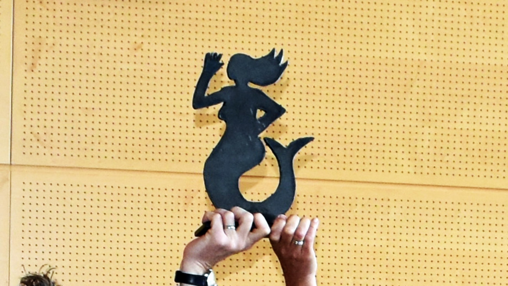 Ein „Emmi för Plattdüütsch in Sleswig-Holsteen“ in Form einer Meerjungfrau wird - getragenen von zwei Händen - in die Luft gestreckt.