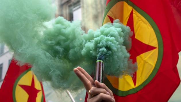 Ein Demonstrant hält eine Rauchfackel mit grünem Rauch und die Fahne der in einigen Ländern verbotenen Arbeiterpartei Kurdistans (PKK) hoch.