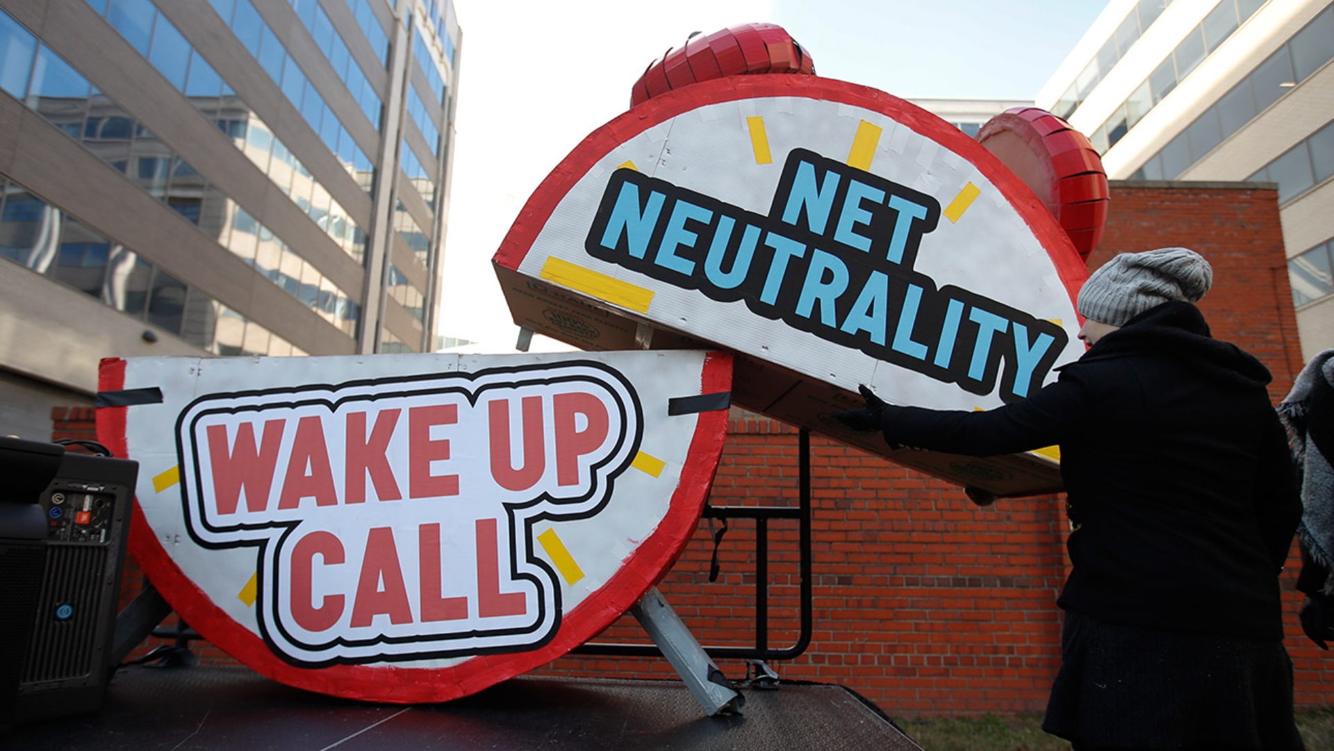 Ein Mann baut bei einer Protestaktion vor dem Gebäude der Telekommunikationsaufsicht FCC in den USA einen riesigen Wecker ab, auf dem "Netzneutralität" und "Weckruf" geschrieben steht.