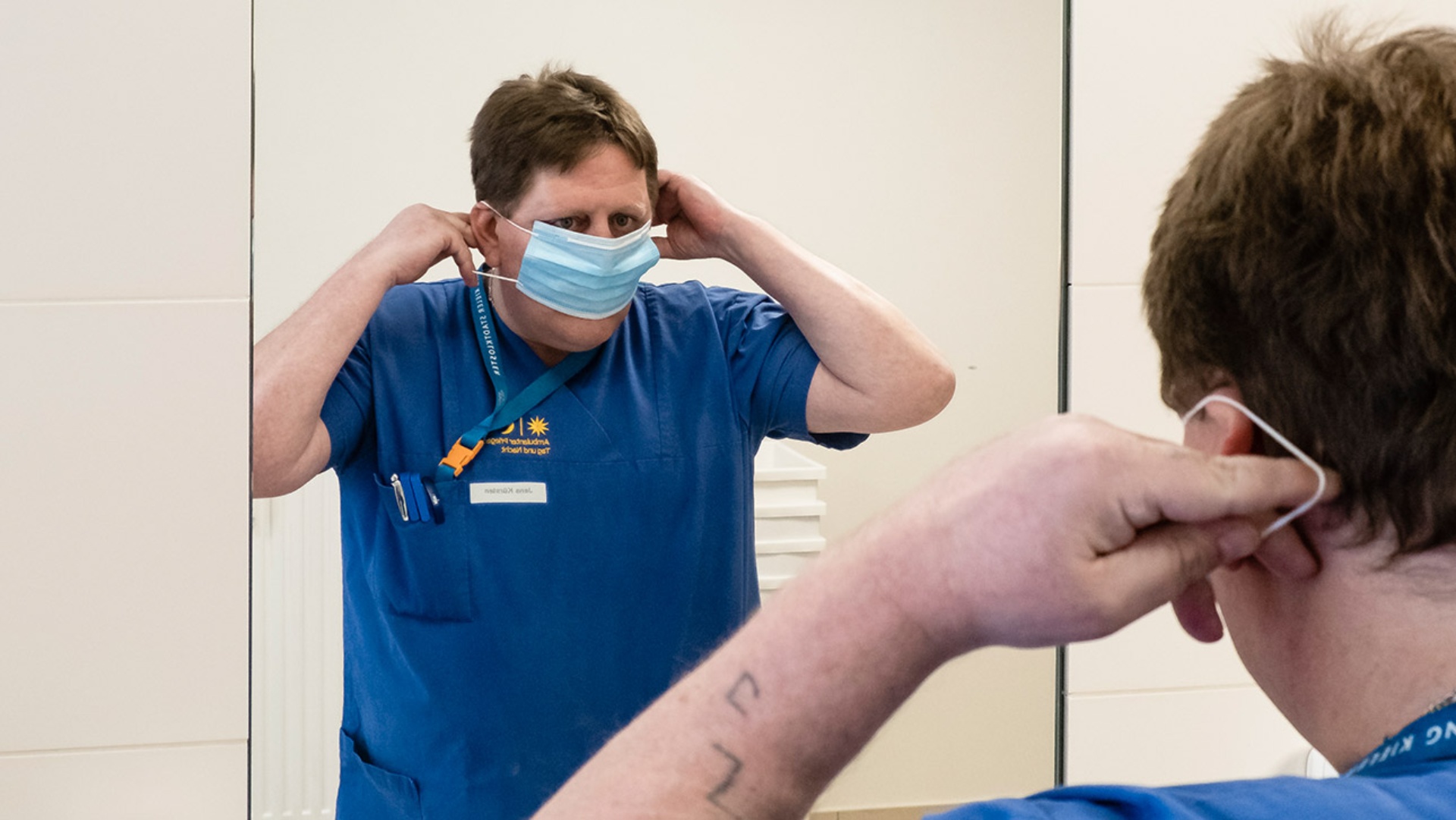 Ein Pfleger in einem Kieler Altenwohnheim erneuert seinen Mundschutz vor dem Spiegel.