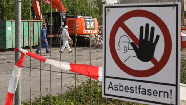 Auf einem Sammelplatz, wo asbestbelasteter Schutt lagert, warnt ein Schild „Asbestfasern!“