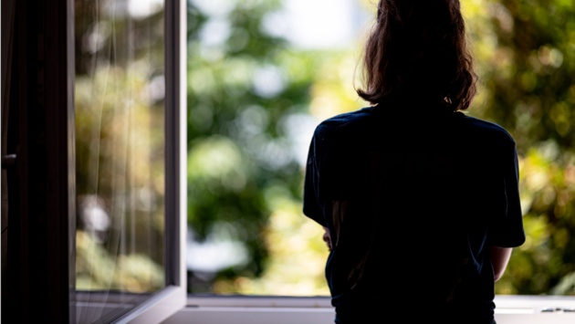 Eine Frau steht in ihrer Wohnung an einem geöffneten Fenster.