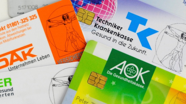 Krankenkassenkarten von mehreren gesetzlichen Krankenkassen liegen auf einem Tisch.