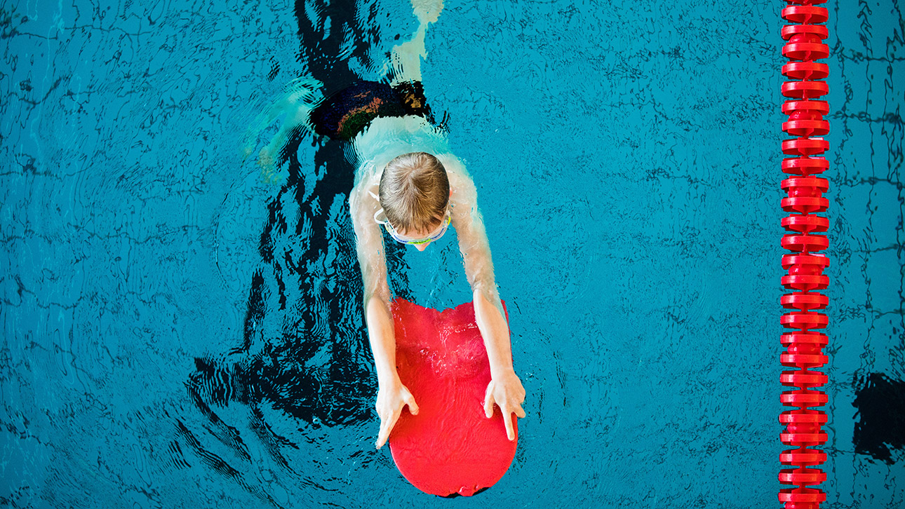 Ein Kind übt im Schwimmunterricht mit einem Schwimmbrett.