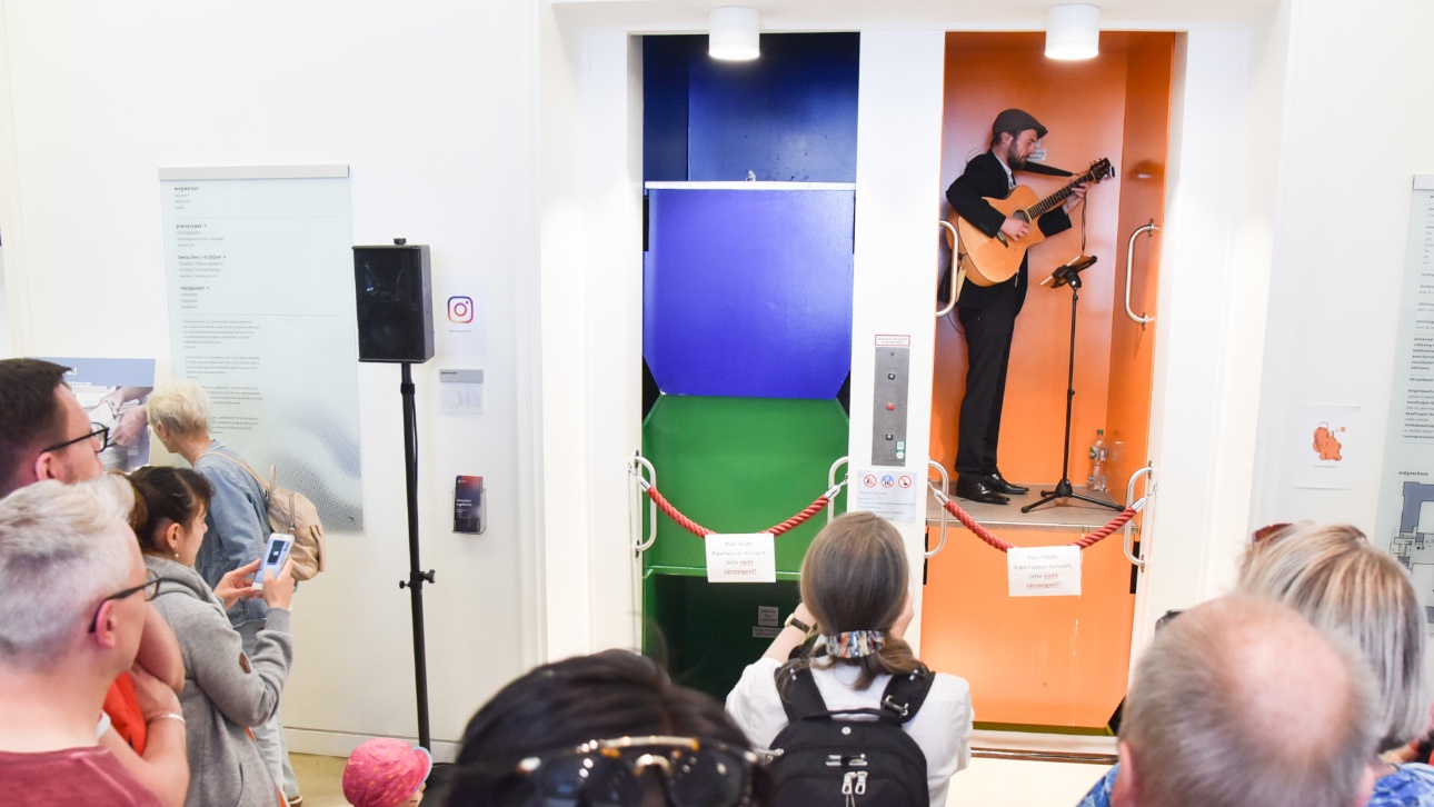 Ein Musiker mit Gitarre spielt vor Publikum in einer Kabine des Paternosters beim Tag der offenen Tür im Landtag Schleswig-Holstein