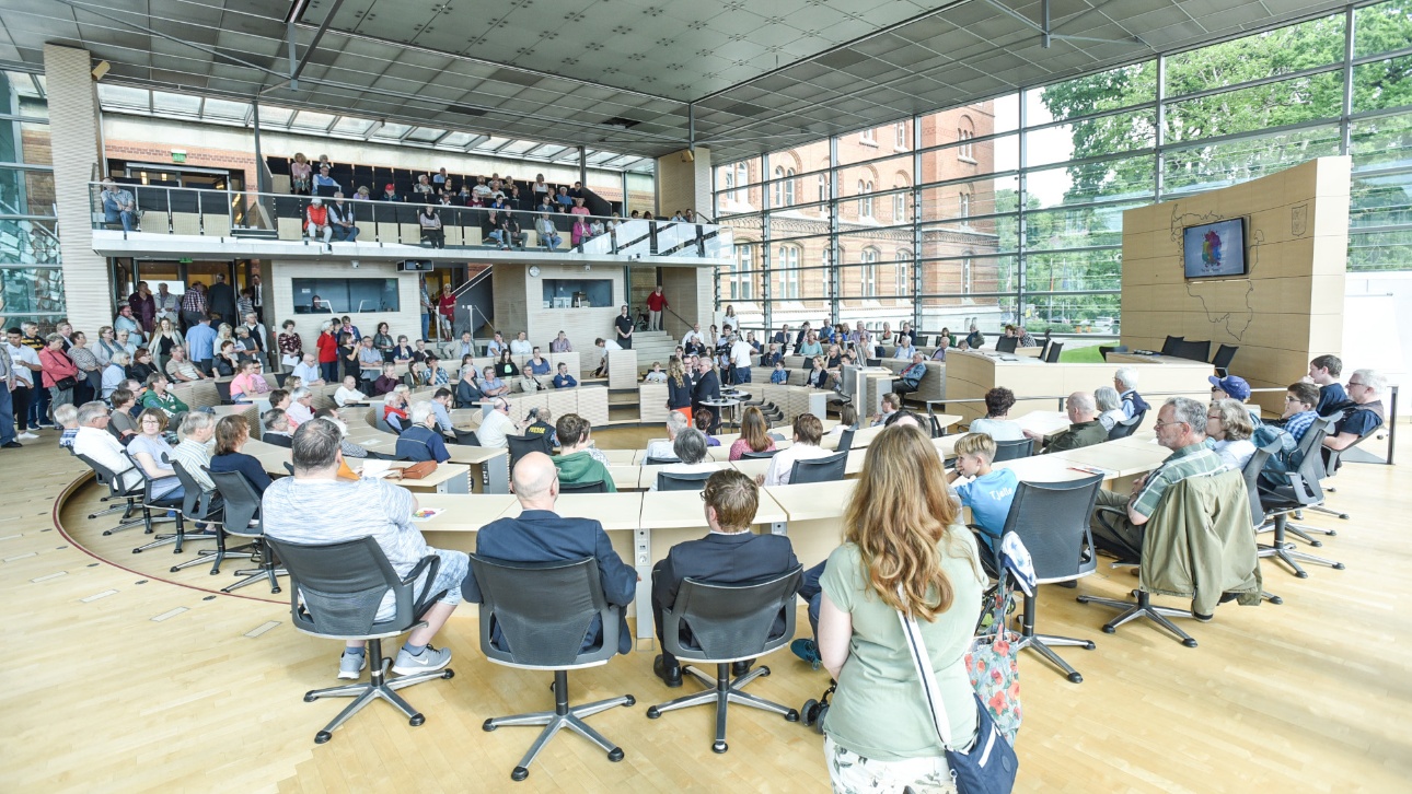 Besucher sitzen bei einem Vortrag des ehemaligen Landtagspräsidenten Klaus Schlie im Plenarsaal beim Tag der offenen Tür im Landtag Schleswig-Holstein