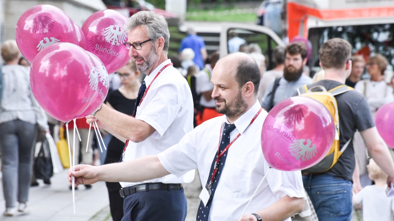 Zwei Männer in weißem Hemd und mit Schlips verteilen lila Luftballons mit der Aufschrift Bundesrat beim Tag der offenen Tür im Landtag Schleswig-Holstein
