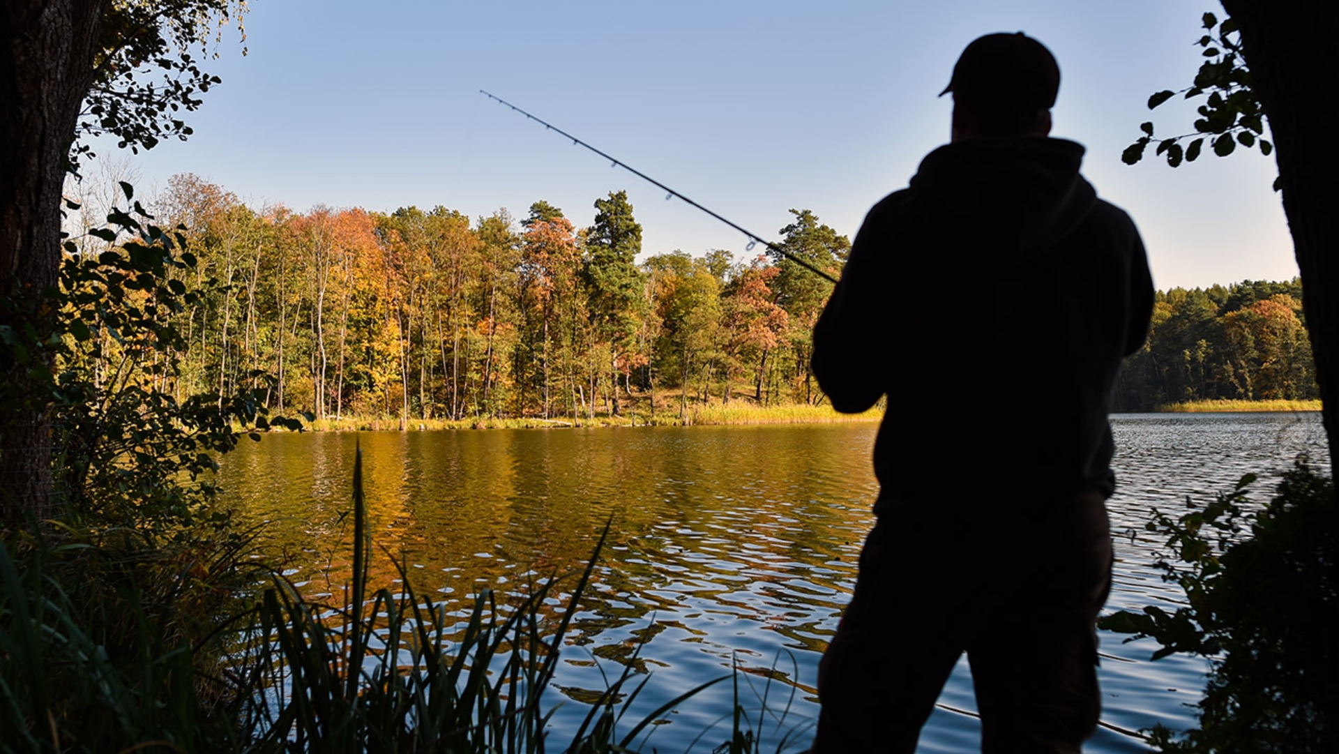 Ein Angler steht mit einer Angel an einem See.