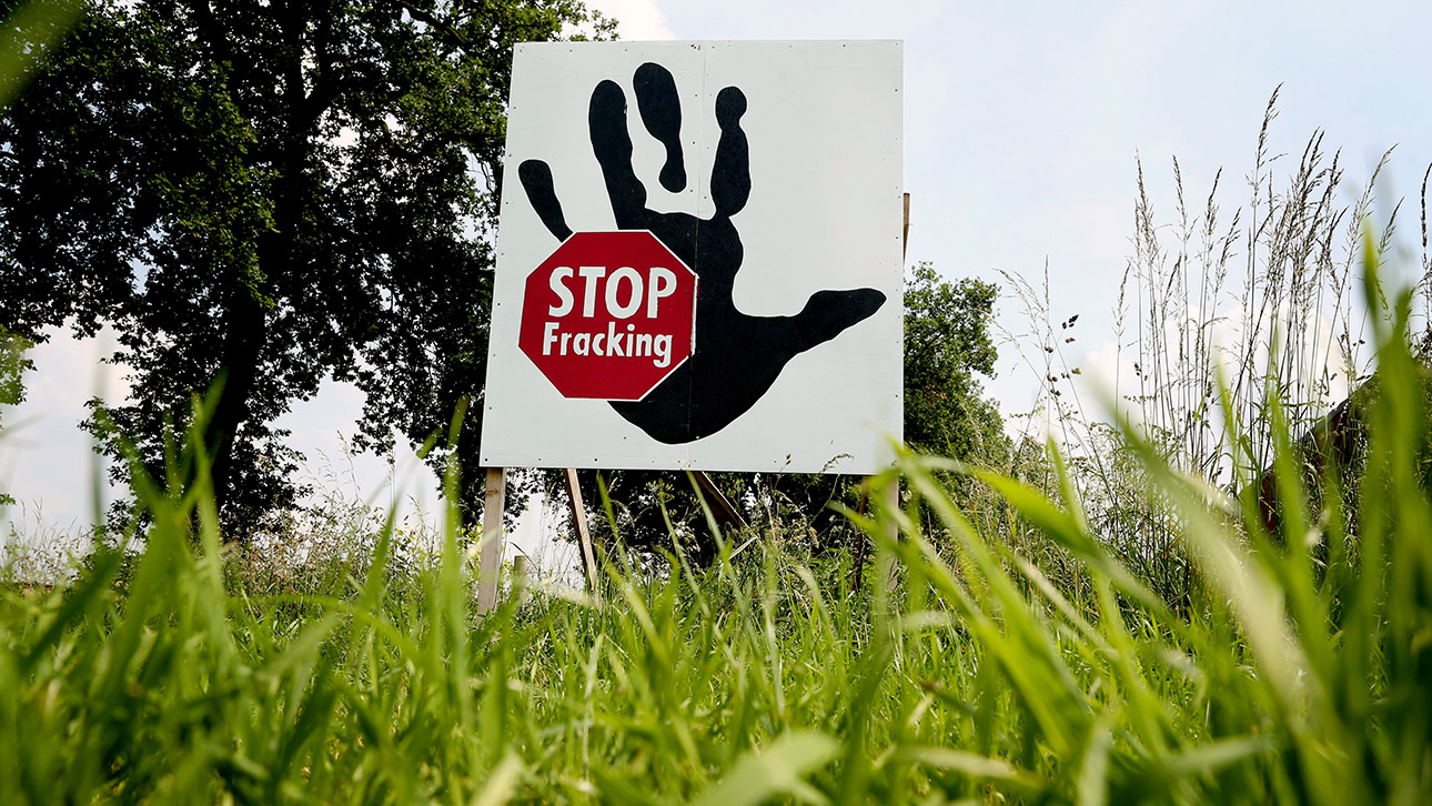 In einem Feld steht ein Plakat mit der Aufschrift „Stop Fracking“ .