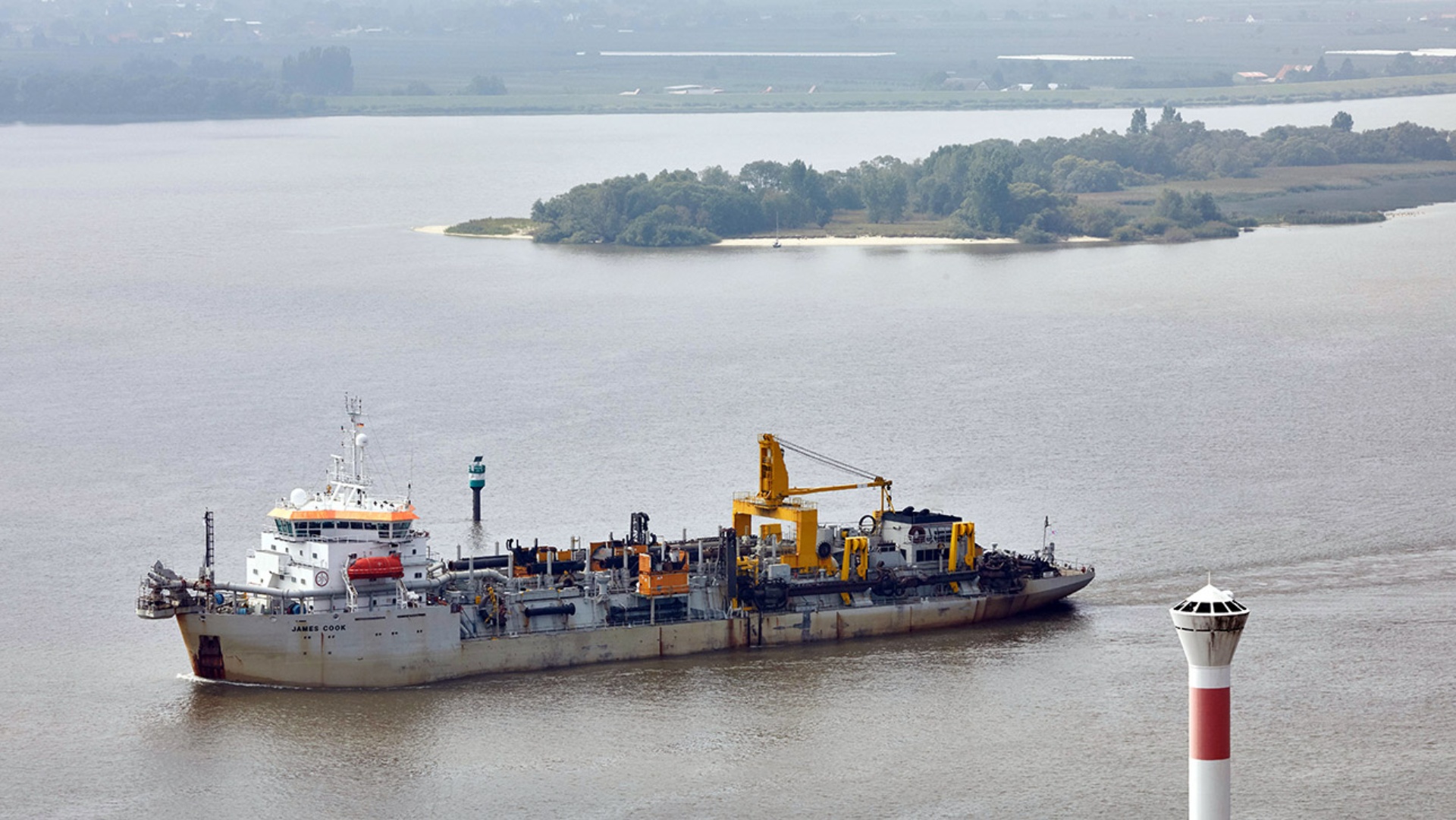 Das Baggerschiff "James Cook" fährt auf der Elbe zwischen dem Leuchtturm Blankenese und einer Insel des Naturschutzgebiets Neßsand.