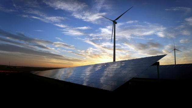 In der Abenddämmerung: Windräder stehen hinter den Solarzellen einer Solarkraftanlage.