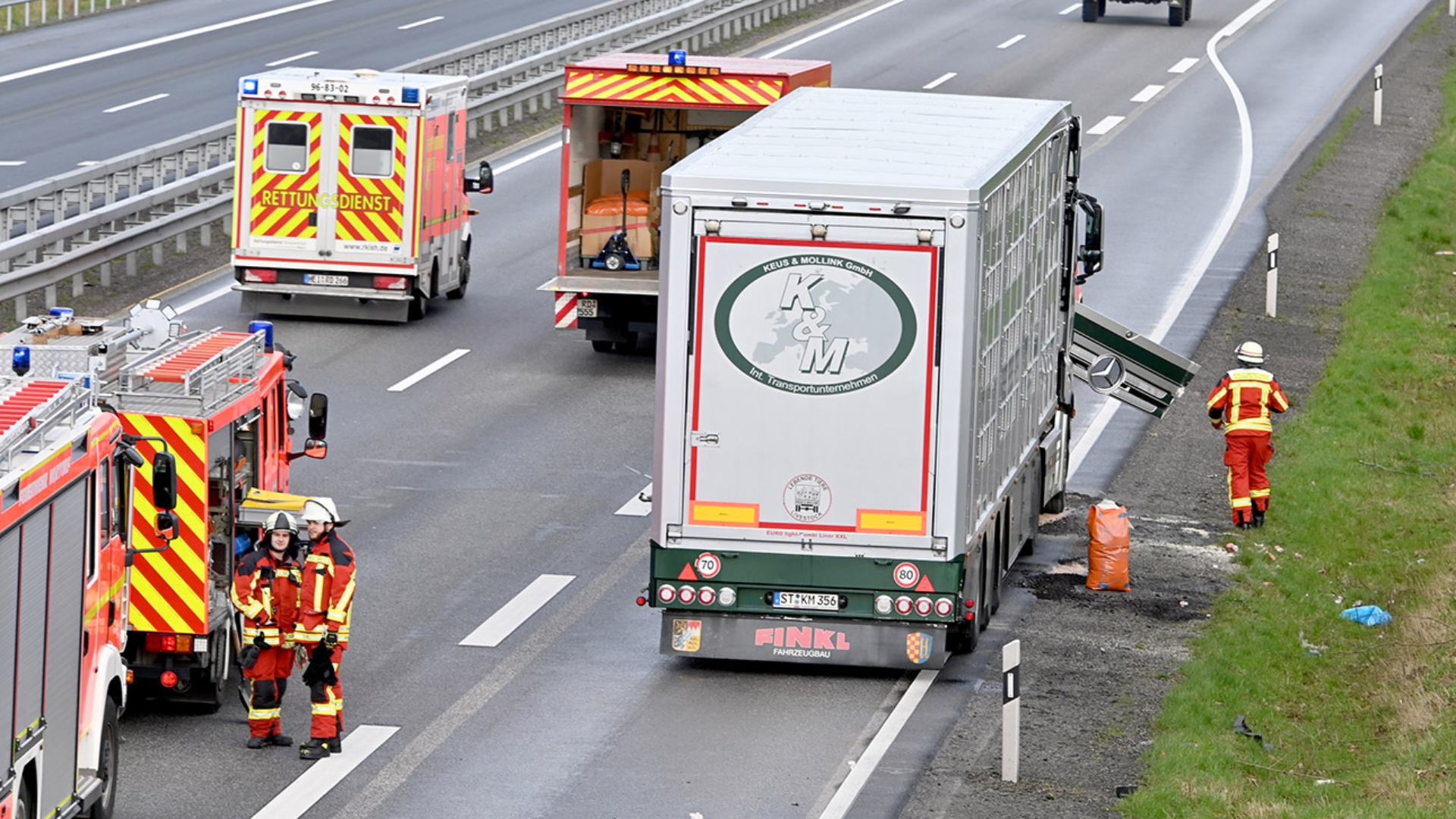 Feuerwehrleute stehen auf der Autobahn 7 an einem Lastwagen, der bei einem Unfall beschädigt wurde.