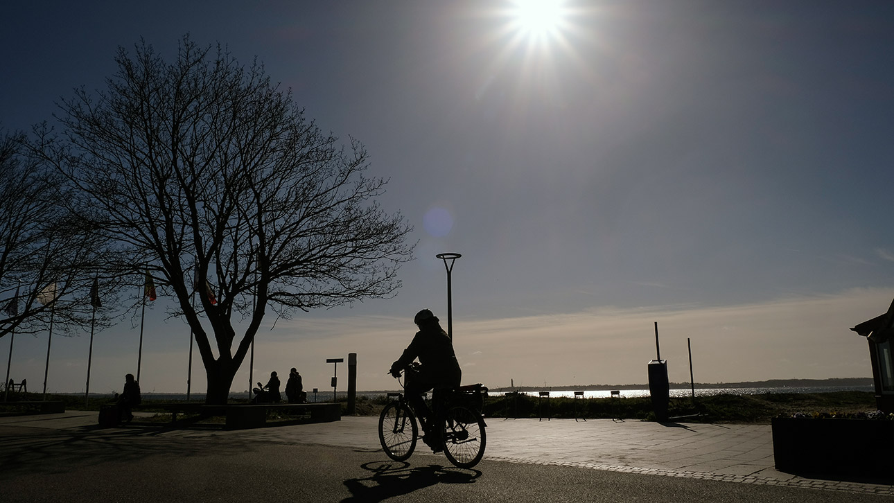 Eine Frau fährt mit dem Fahrrad im Gegenlicht an der Ostsee entlang.