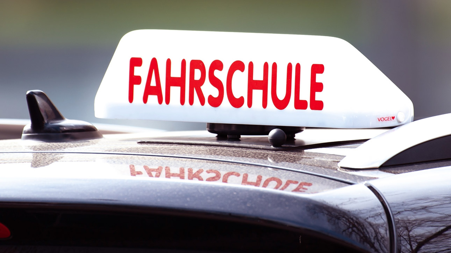 Ein Schild mit der Aufschrift "Fahrschule" ist auf einem Fahrschulauto befestigt.