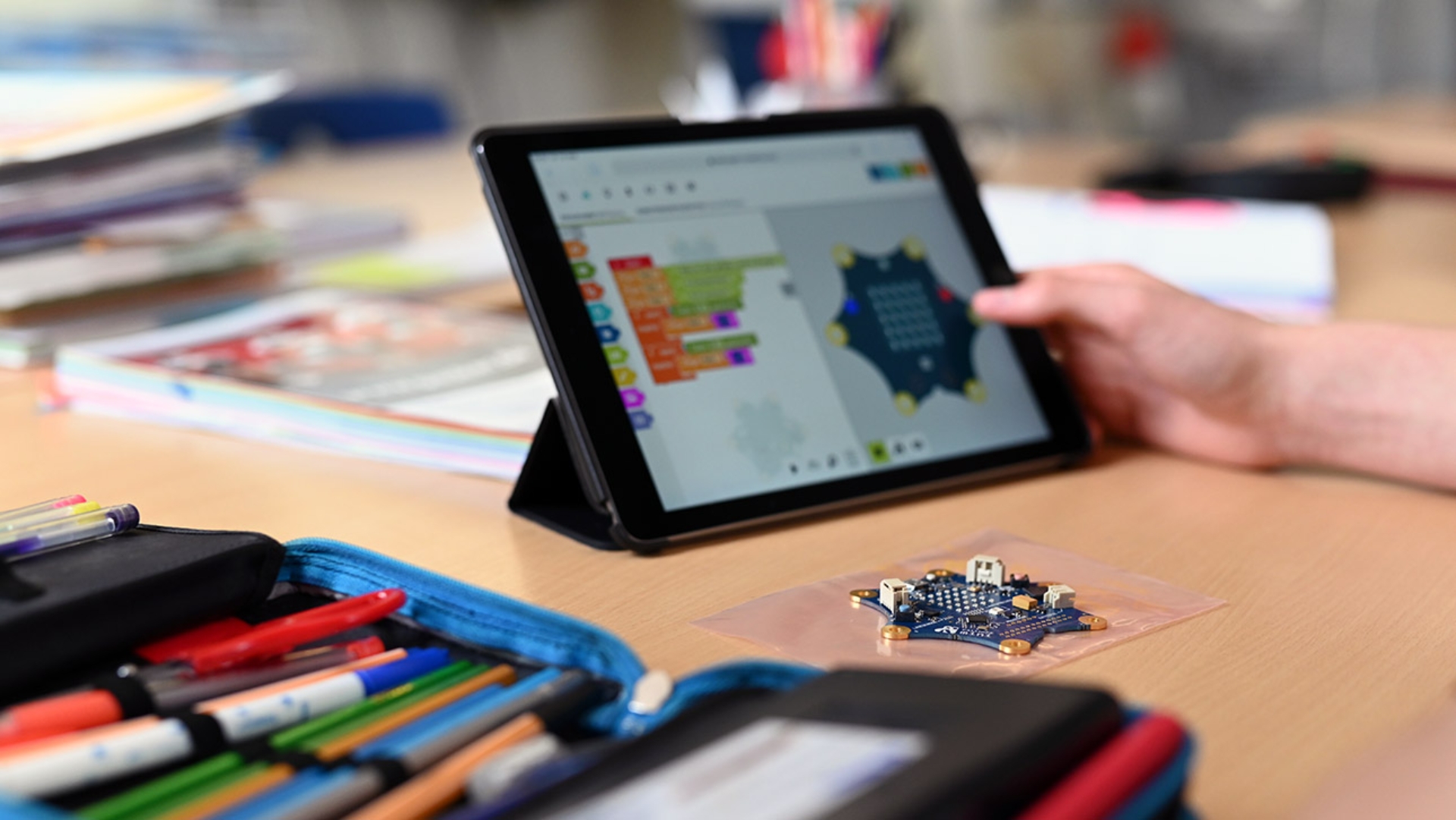 Auf einem Schultisch ist ein kleiner Laptop mit einer Grafik aufgerichtet. Davor steht ein kleines Modell und davor liegt eine Federtasche mit Schreibstiften.