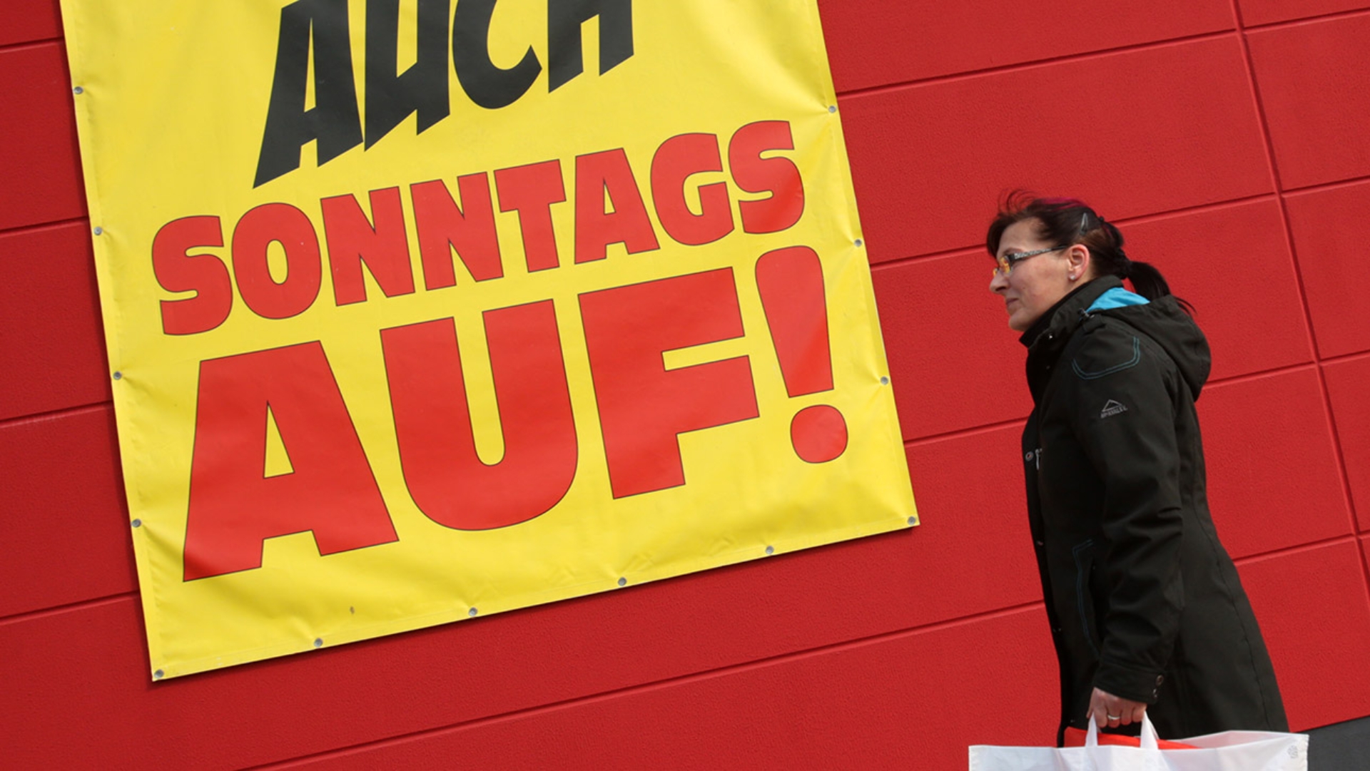 Frau vor einem Werbeschild zur Sonntagsöffnung