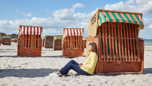 Eine Frau lehnt an einem Strandkorbund genießt die Sonne am Strand.