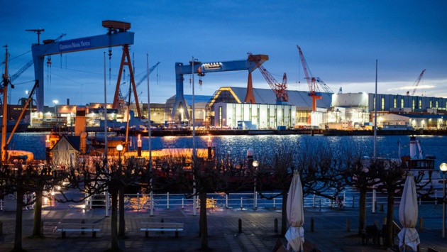 Das Foto zeigt das beleuchtete Werftgelände von ThyssenKrupp Marine Systems am Ufer der Förde bei Sonnenaufgang.