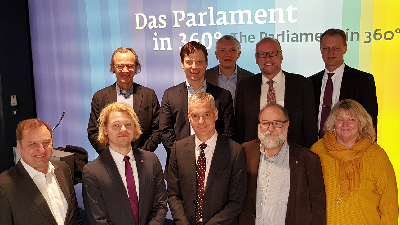 Die Mitglieder des Europaausschusses stehen in Fotostudio in Berlin. Im Hintergrund steht auf einer Leinwand Parlament in 360 Grad.