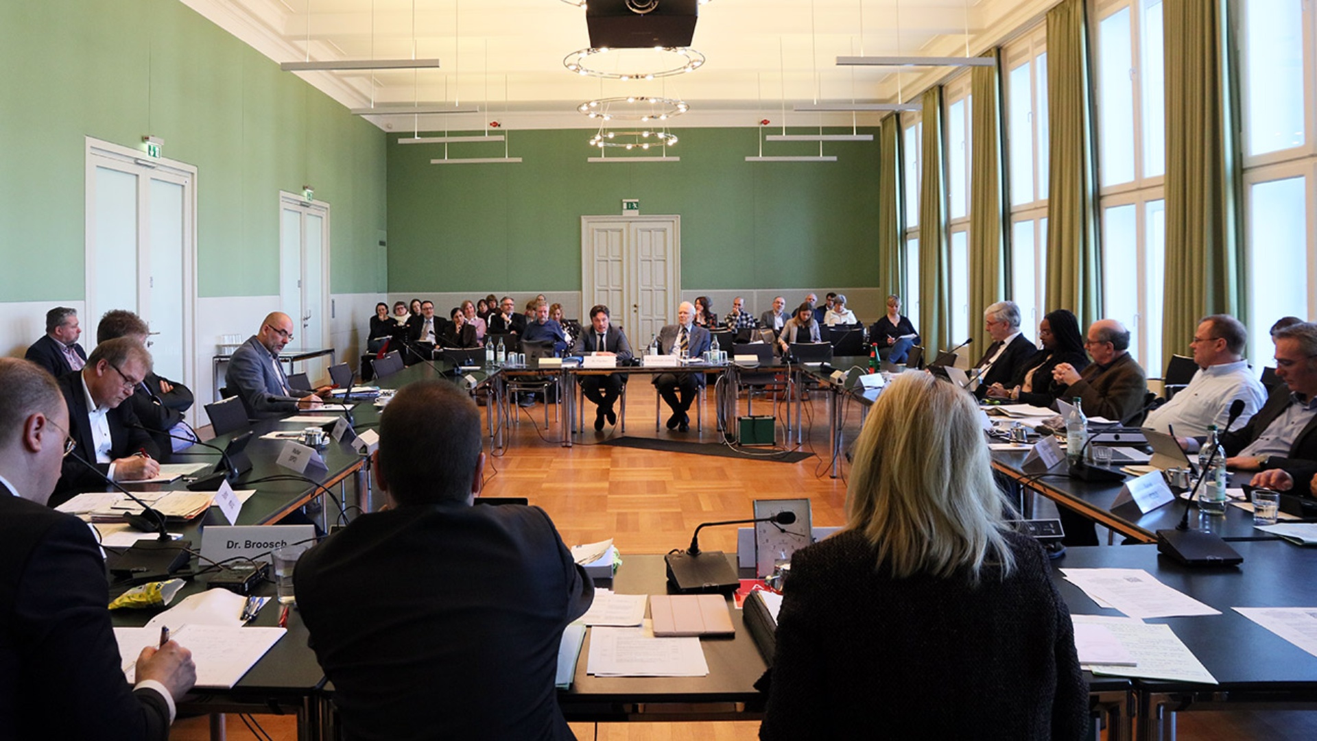 Die Mitglieder des Innen- und Rechtsausschusses sitzen rechts und links an Tischen. Im Hintergrund sind zahlreiche Zuschauer zu sehen.