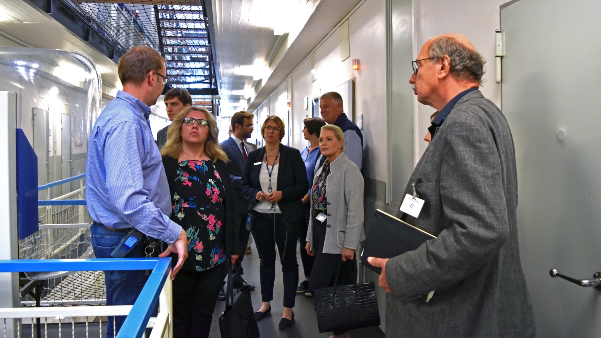 Eine Gruppe Abgeordneter steht auf einem Flur in der JVA Lübeck und lauscht einem Mitarbeiter.