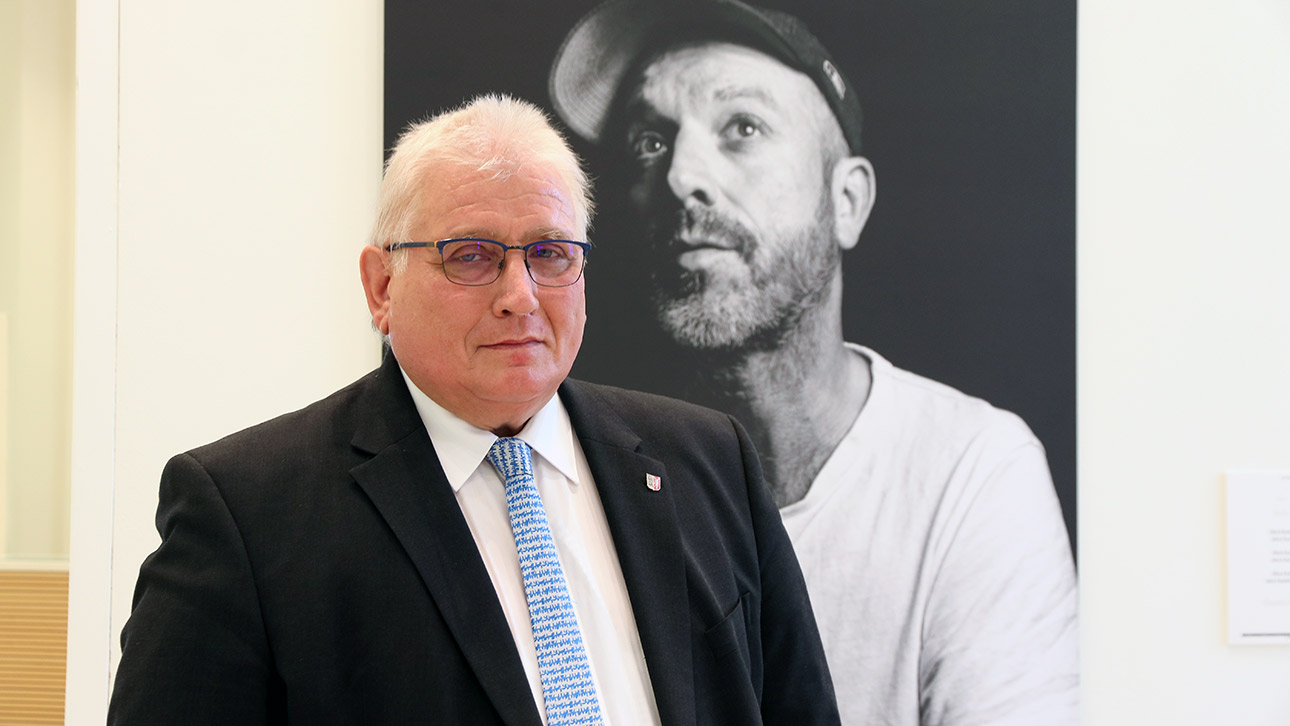 Landtagspräsident Schlie steht vor einem Porträt des Künstlers Jan Plewka.