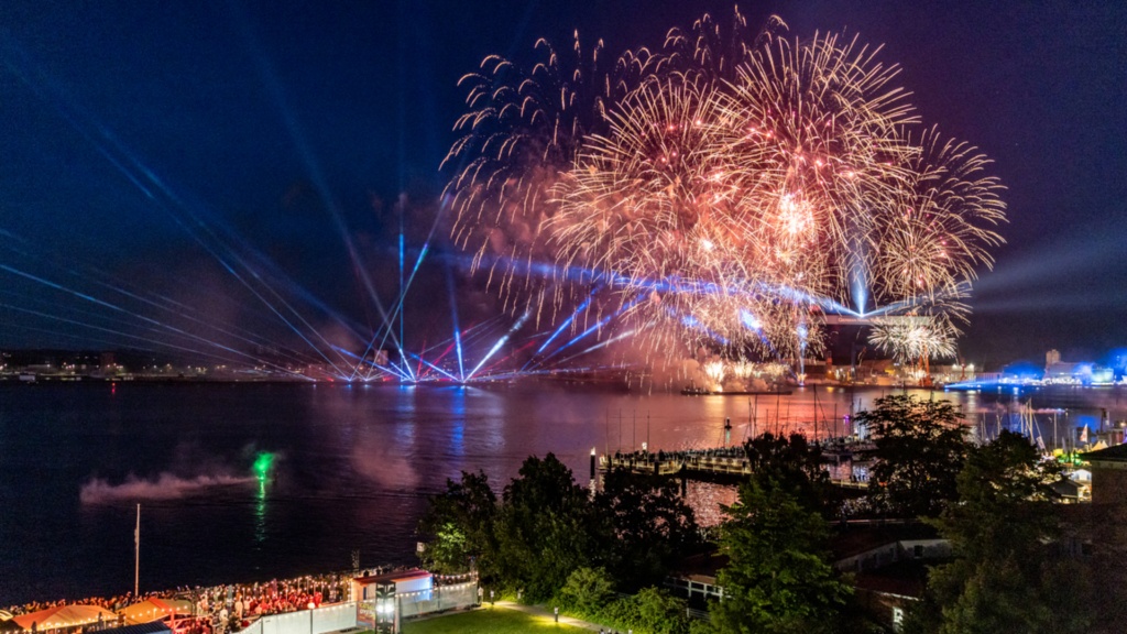 Das Abschlussfeuerwerk zur Kieler Woche 2025 über der Kieler Förde, beobachtet aus einem Fenster in einem oberen Stockwerk des Landeshauses