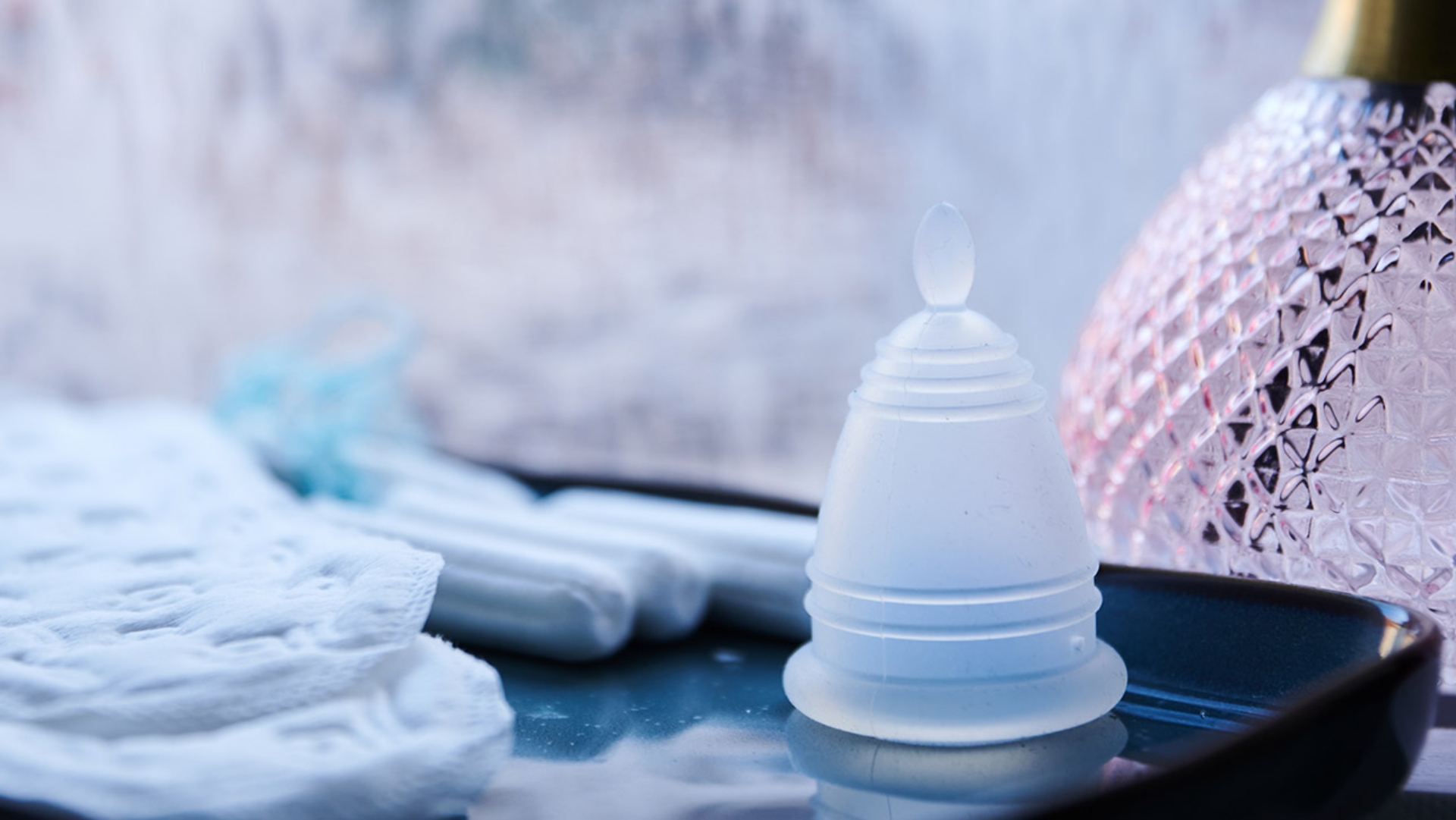 Eine Menstruationstasse, Slipeinlagen und Tampons liegen in einem Badezimmer. 