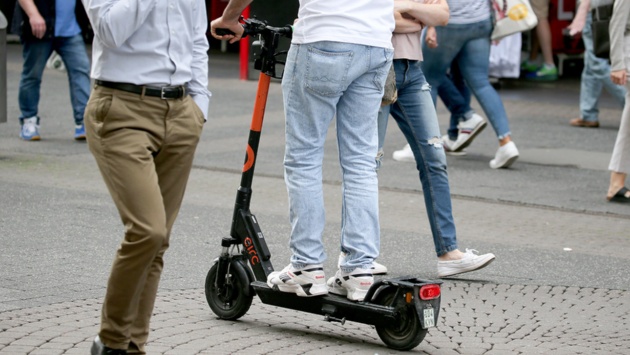 Mit einem Elektro Tretroller fährt ein Mann durch die Fußgängerzone.