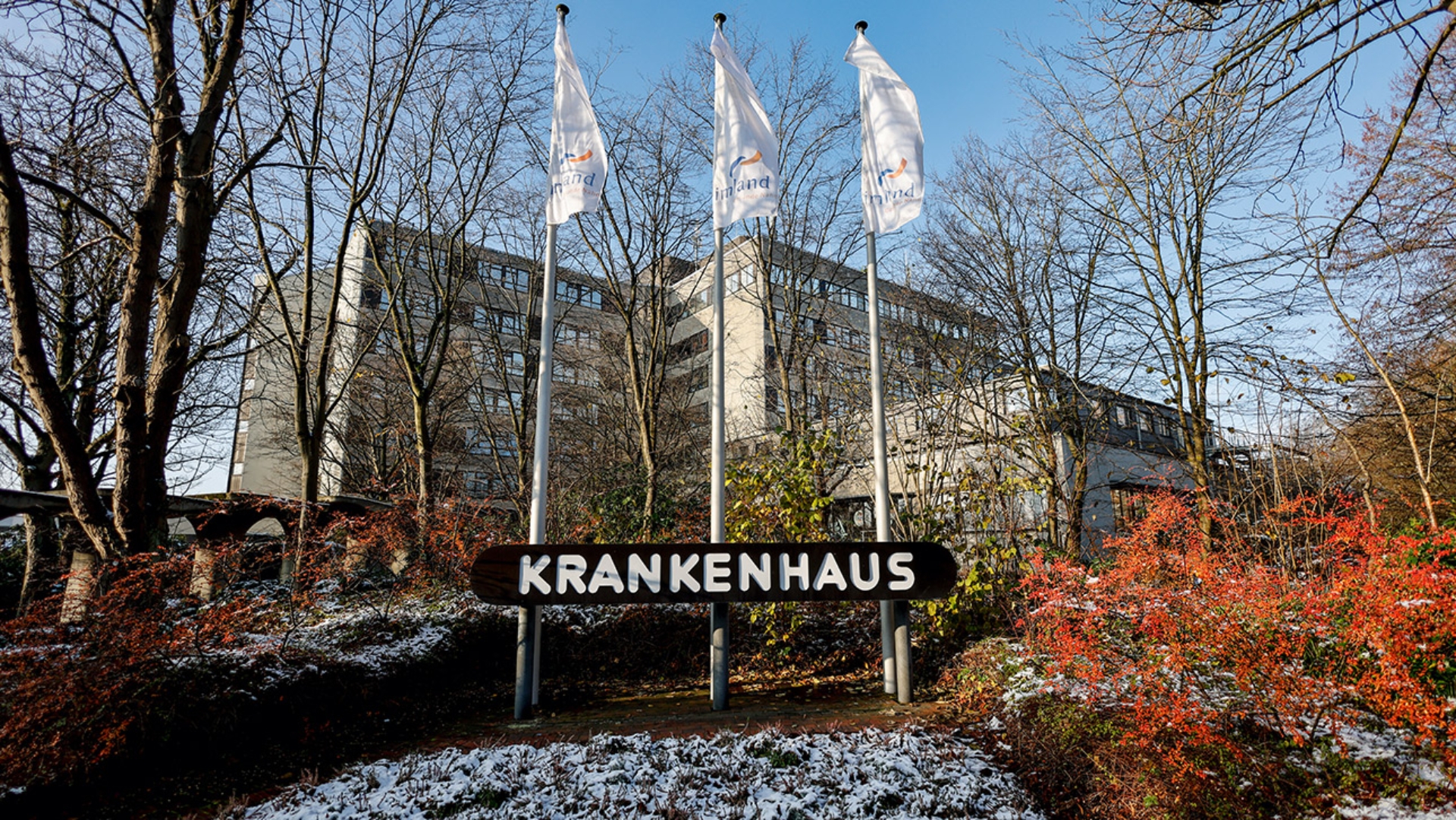 Fahnen mit dem Klinik-Logo wehen vor dem Haupteingang der Imland-Klinik in Rendsburg. Die Imland Kliniken haben ihre Insolvenz gemeldet.